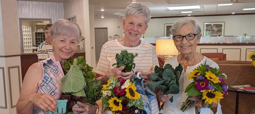 Three residents holding fresh produce and flowers