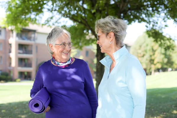 Two senior women chatting outdoors with a yoga mat