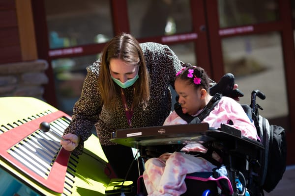 A caregiver helping a child in a wheelchair outdoors