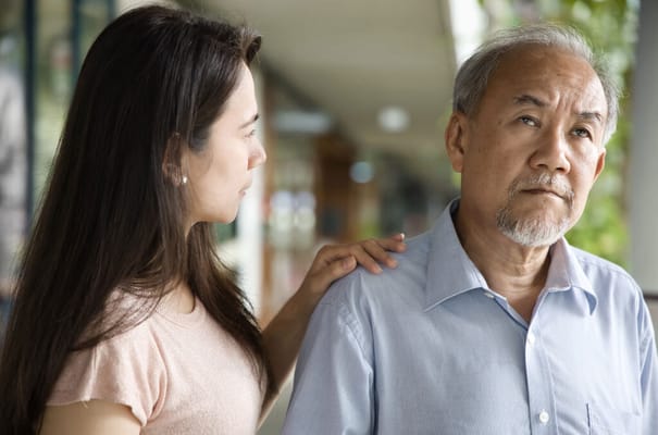 A woman comforting an elderly man outdoors
