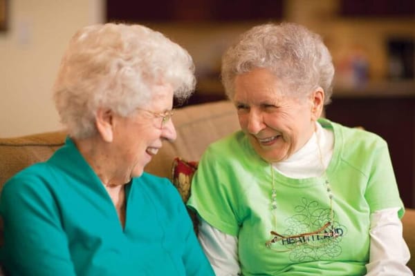Two senior women laughing together in a cozy living room