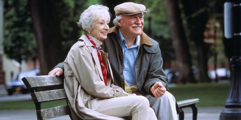 An elderly couple sitting on a park bench
