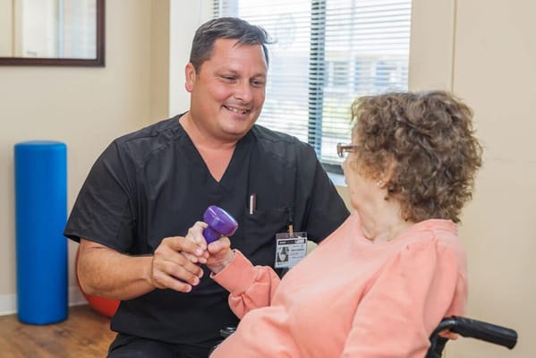 Staff assisting a resident with light weights in a therapy session