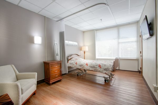 A cozy private resident room with a bed and chair