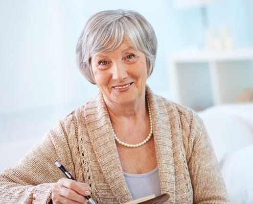 Senior woman smiling while writing in a notebook