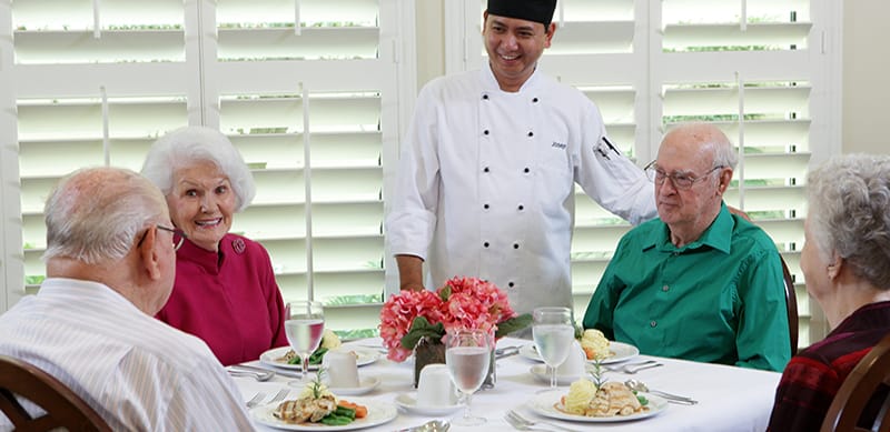 Residents enjoying a meal with a chef in a dining room
