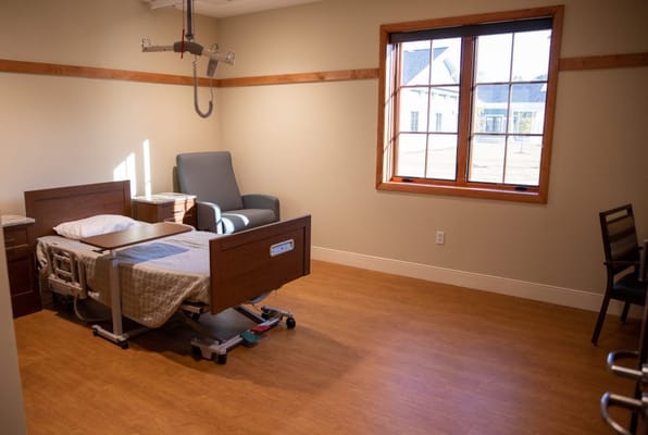 Well-lit private resident room with bed and chair