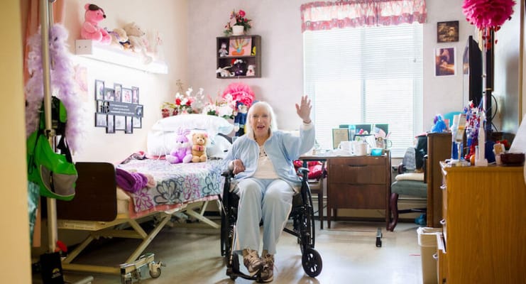 A resident in a wheelchair waving in their room