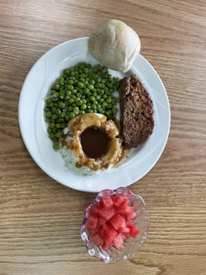 Plate of meatloaf, green peas, and watermelon