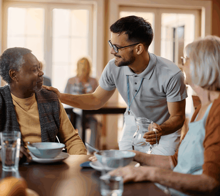 A staff member serving water to residents in a dining setting