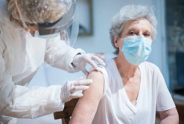 A resident receiving a vaccine from a caregiver