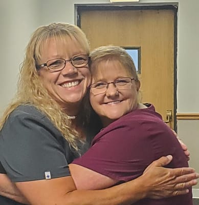 Two staff members smiling and hugging in an interior hallway