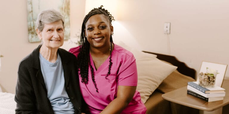 Senior resident and caregiver smiling together in a room