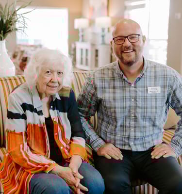 A resident and staff member smiling together on a sofa