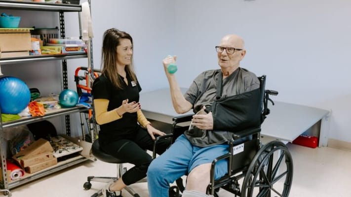 A resident exercising with a staff member in a therapy room