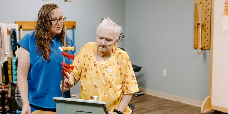 A caregiver assists a resident in a therapy room