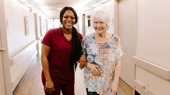 Healthcare worker and resident smiling in a hallway