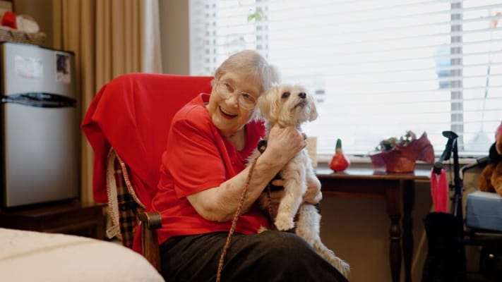 Resident smiling and holding a dog in a cozy room