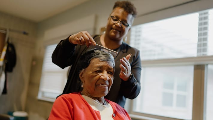 Staff providing hair care to a resident in an interior setting