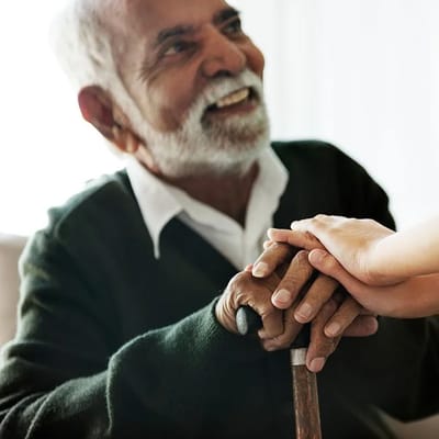 Elderly man smiling, holding hands with a caregiver