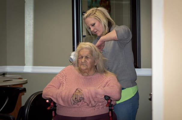 A caregiver styling a resident's hair in a lounge.