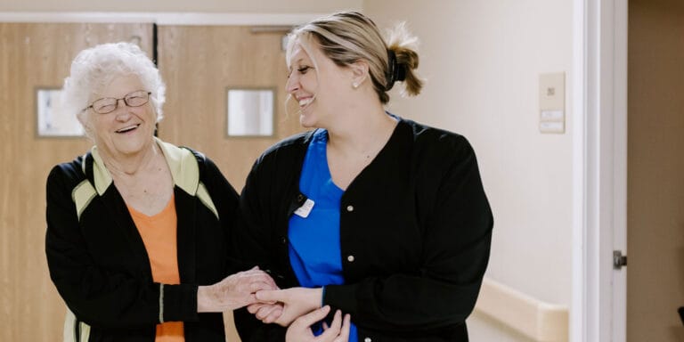 A staff member walking with a smiling resident