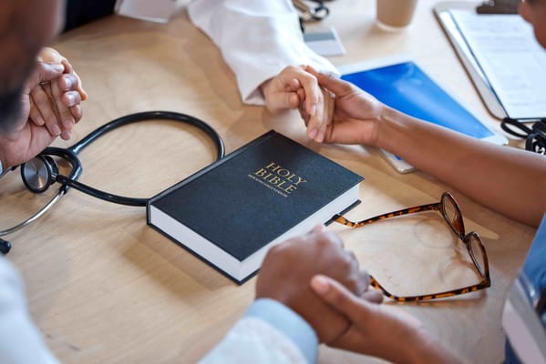 Hands gathered around a Bible on a table