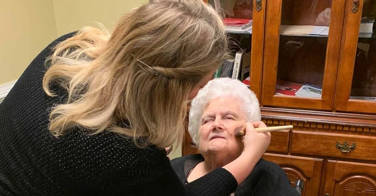 Caregiver applying makeup to a senior woman