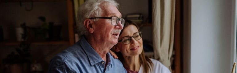 Elderly man and caregiver smiling by a window