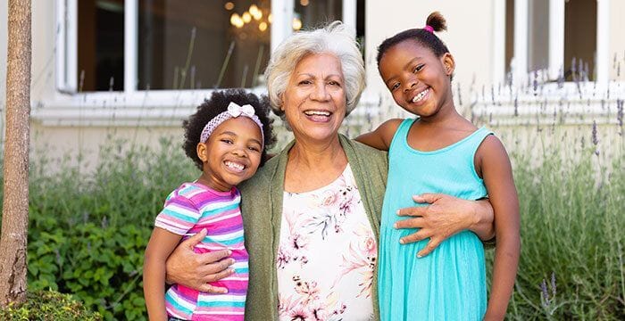 A smiling senior woman with two young girls in a garden