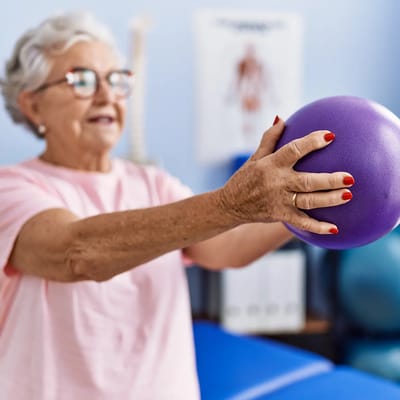 Senior woman exercising with a purple ball in therapy room