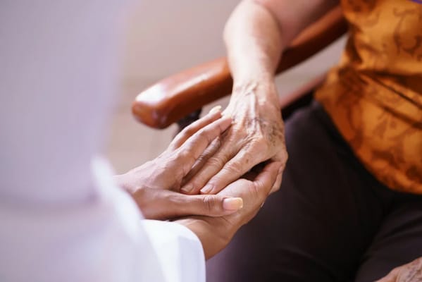 A caregiver holding a senior's hand in a warm interaction