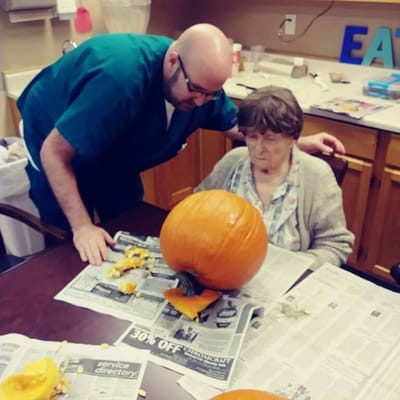 Resident and staff member carving a pumpkin indoors