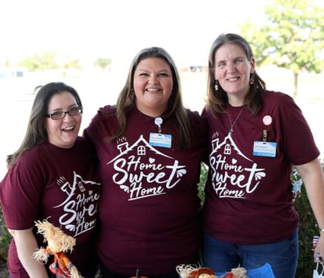 Three staff members smiling outside with community decor