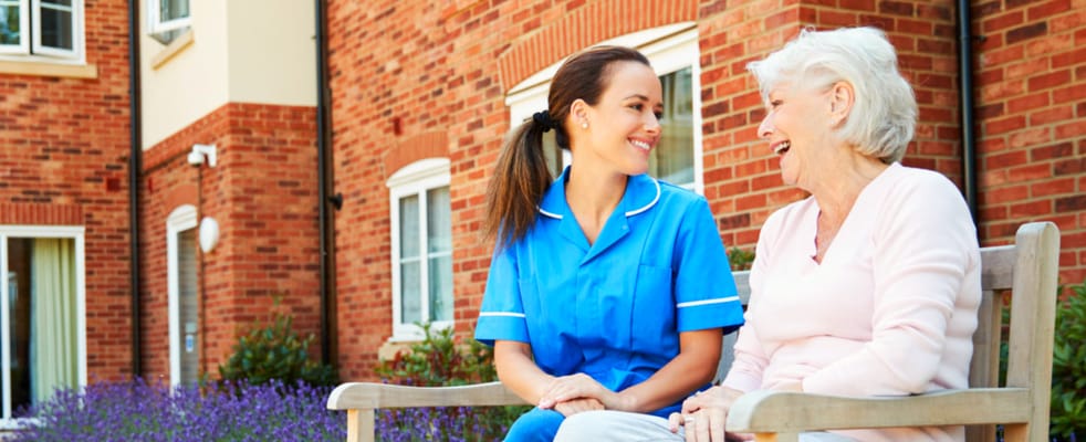 A caregiver and resident laughing outdoors on a bench