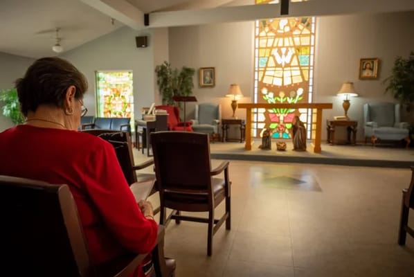 A woman sitting in a quiet chapel with stained glass.