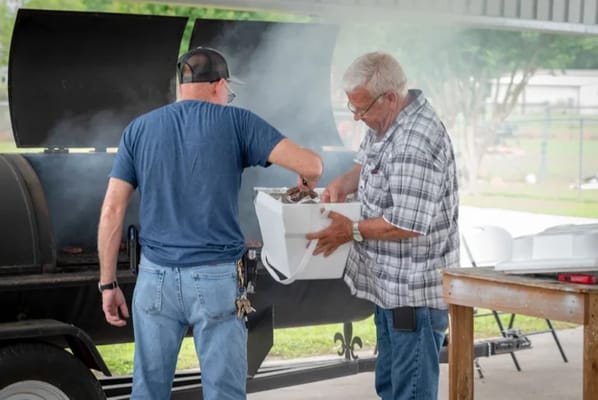 Two men grilling food outdoors at a community event