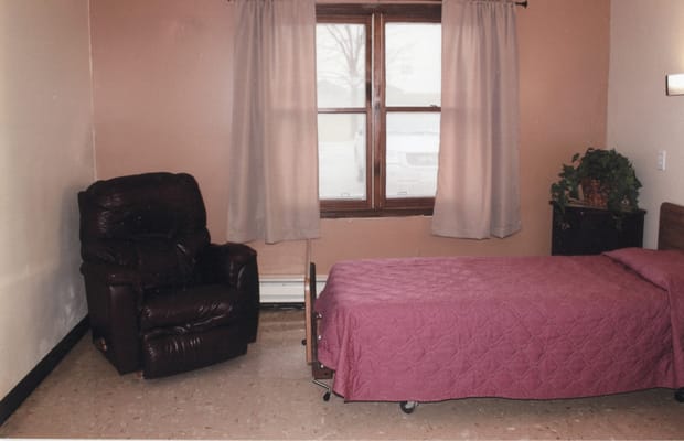 Simple private resident room with a bed and armchair