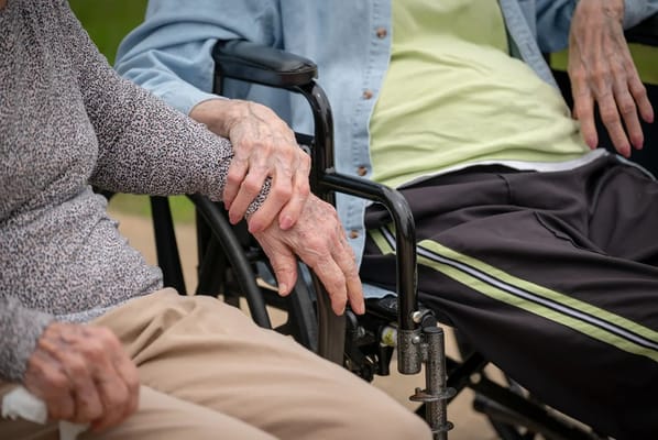 Two elderly residents holding hands in wheelchair
