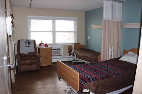 Private resident room with two beds and a chair