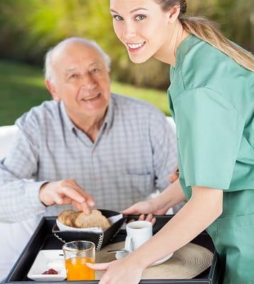 Caregiver serving breakfast outdoors to elderly man