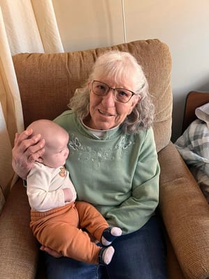 Resident holding a baby, smiling in a cozy chair
