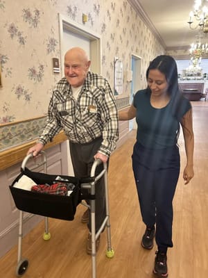 A resident walking with staff assistance in a hallway