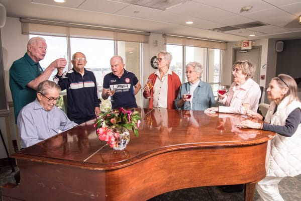 Seniors celebrating together at a piano in a lounge area
