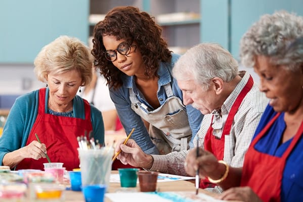 Residents participating in a painting activity with staff guidance