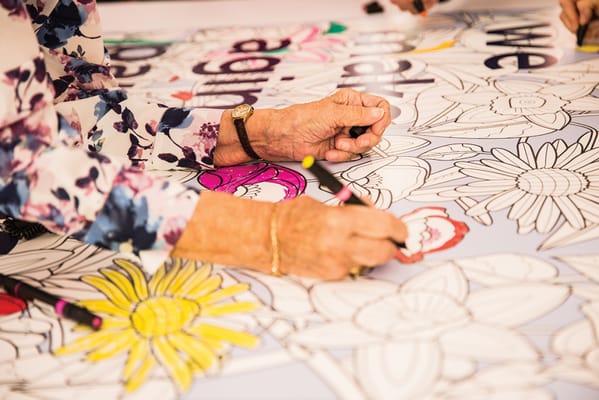 Hands coloring a large mural with flowers