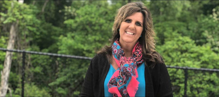 A staff member smiling outdoors in a garden setting