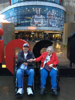 Two seniors in wheelchairs outside a large building