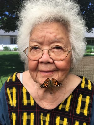 An elderly woman with a butterfly on her chest outdoors
