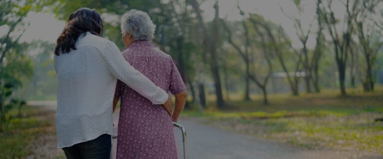 A caregiver assisting an elderly woman in a park
